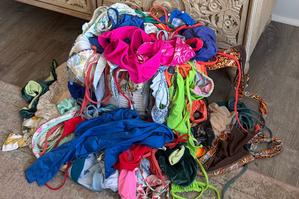 Pile of colorful bikinis and swimwear fabric on a textured surface next to a decorative wooden cabinet.
